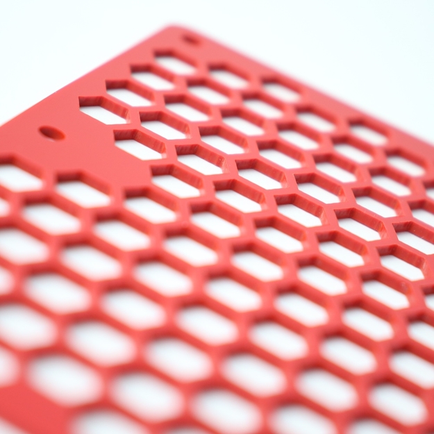 Small, hexagonal holes into a red acrylic panel