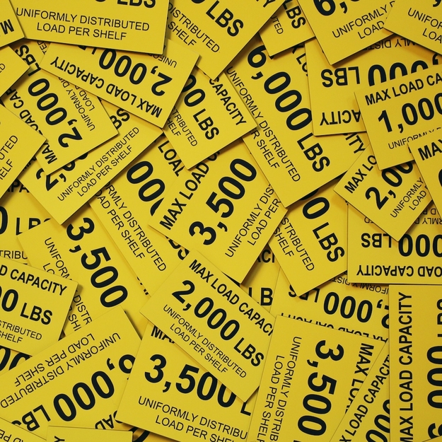 Pile of assorted yellow/black placards indicating the max load capacities for shelving